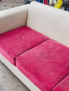Sofa warna merah muda dengan debu dan noda yang terlihat sebelum dibersihkan.